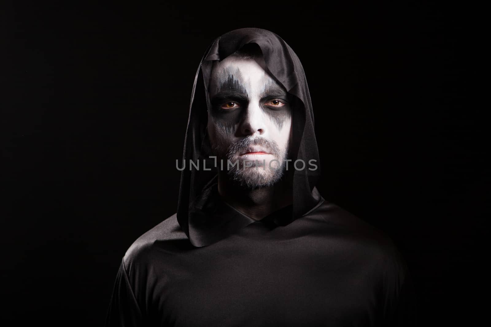 Portrait of man wearing demon make up for halloween party isolated over black background.