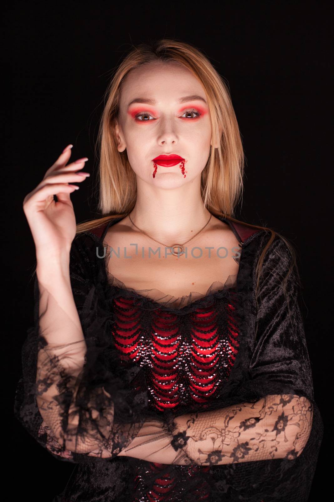 Blond woman dressed up like a vampire with blood on his lips over black background. Halloween costume.