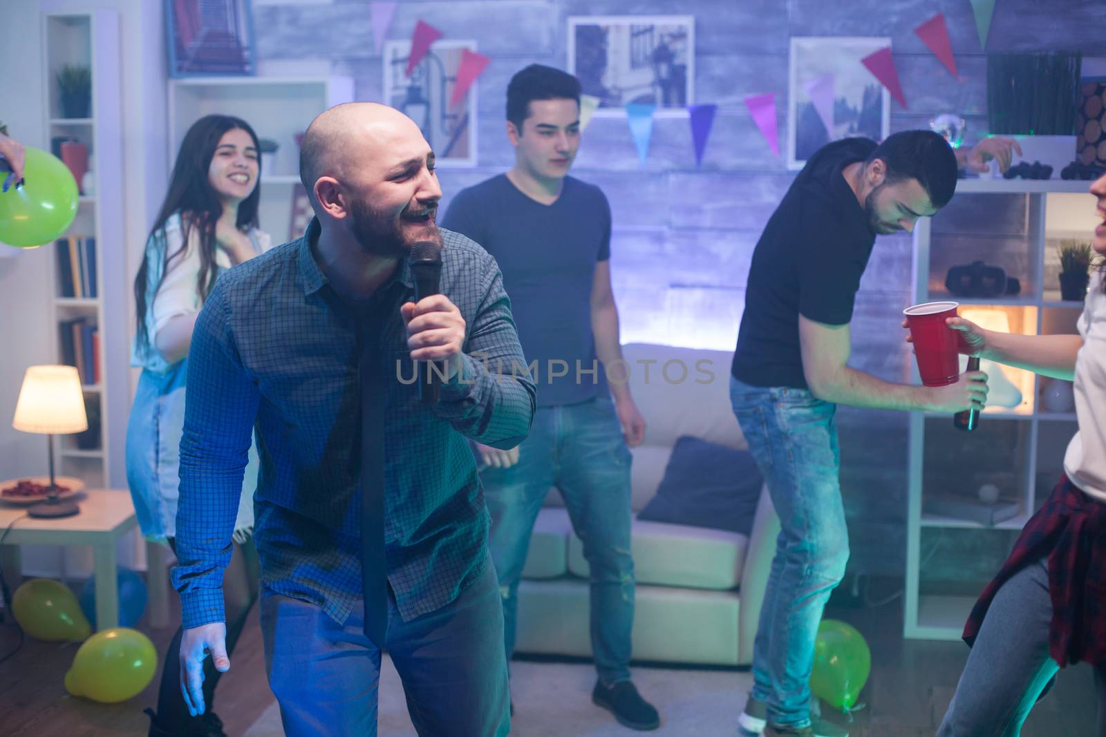 Young caucasian man singing on microphone for his friends entertainment at the party.