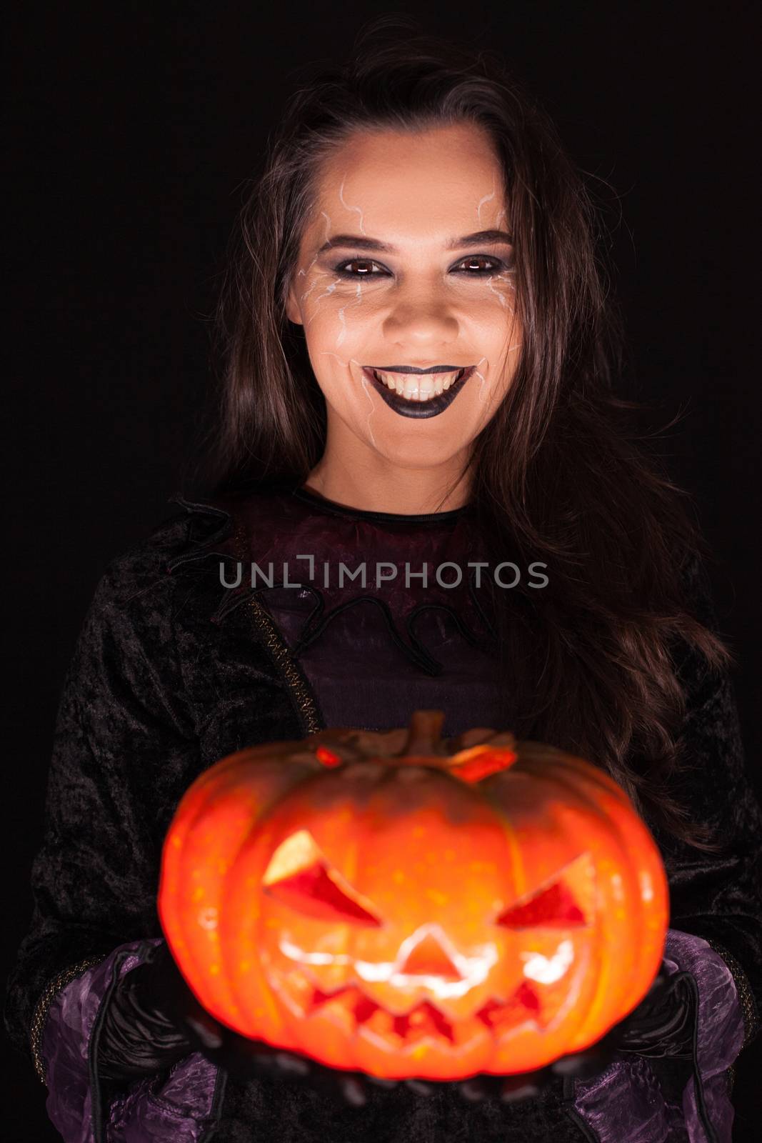 Beautiful woman wearing witch outfit for halloween holding a spooky pumpkin over black background.