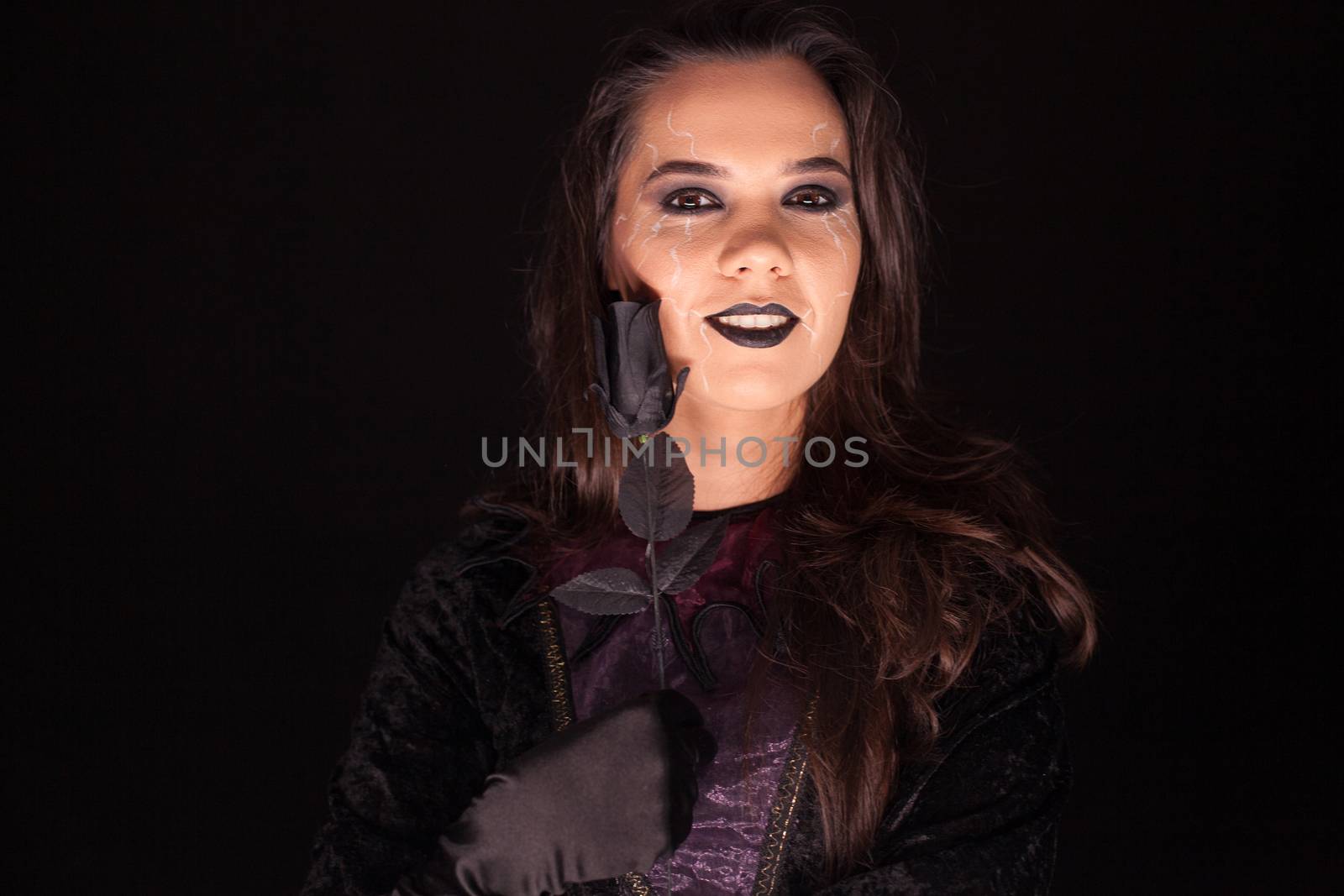 Attractive young woman dressed up like a gothic witch with a rose over black background for halloween.