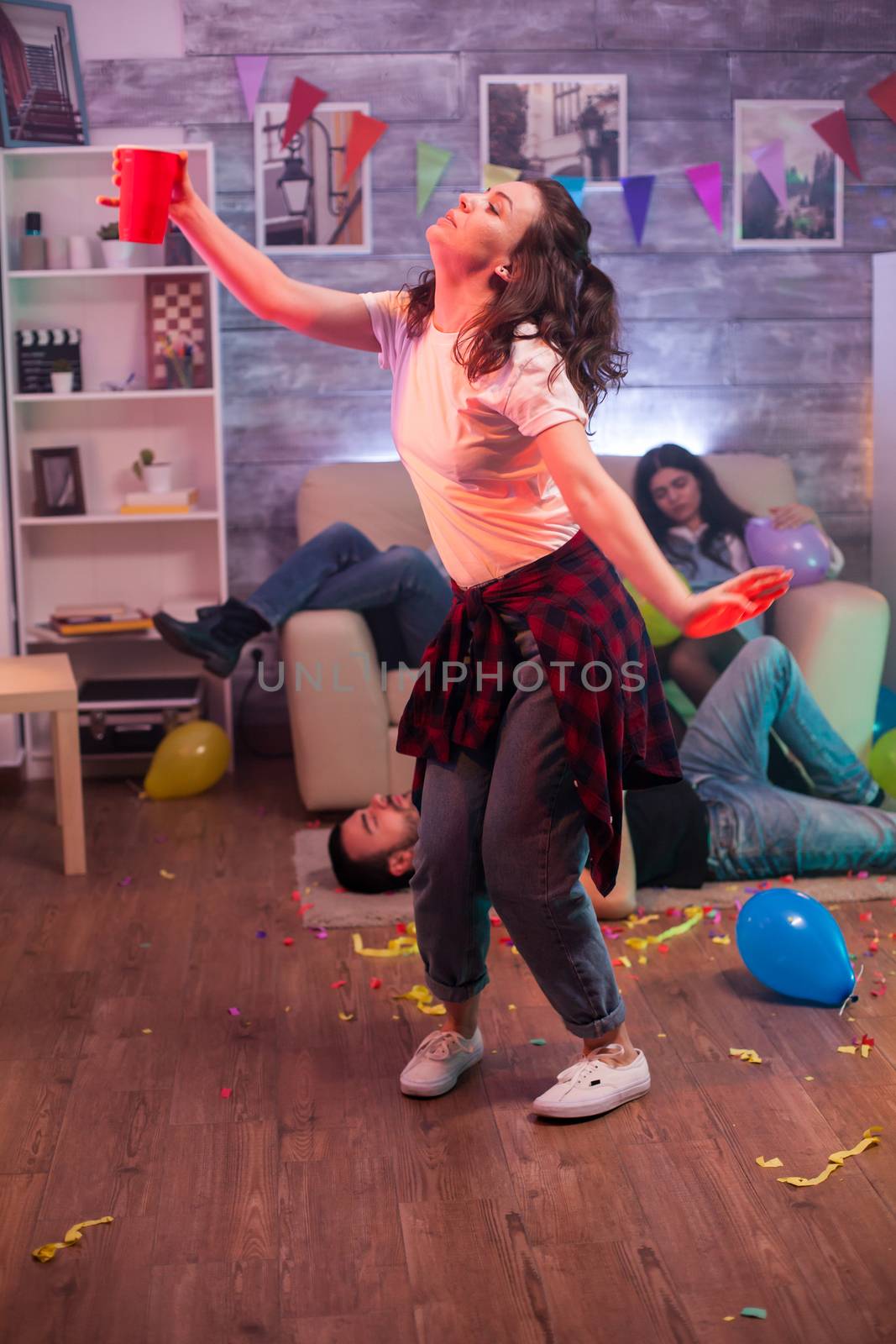 Young woman dancing alone at friends party. Group of friend lying on the floor.
