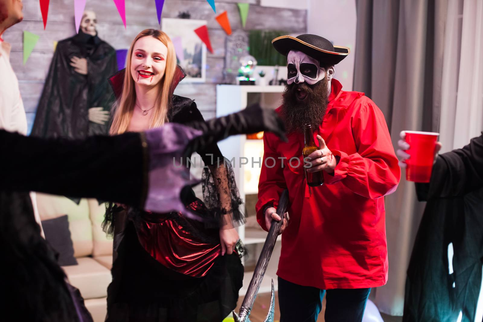 Man and woman dressed up like a pirate and vampire at halloween celebration with their friends.