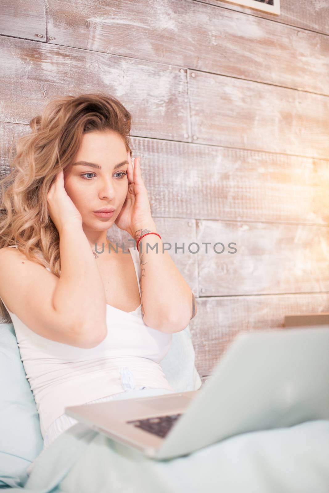 Attractive woman in pajamas having a headache while workin on laptop sitting on bed.