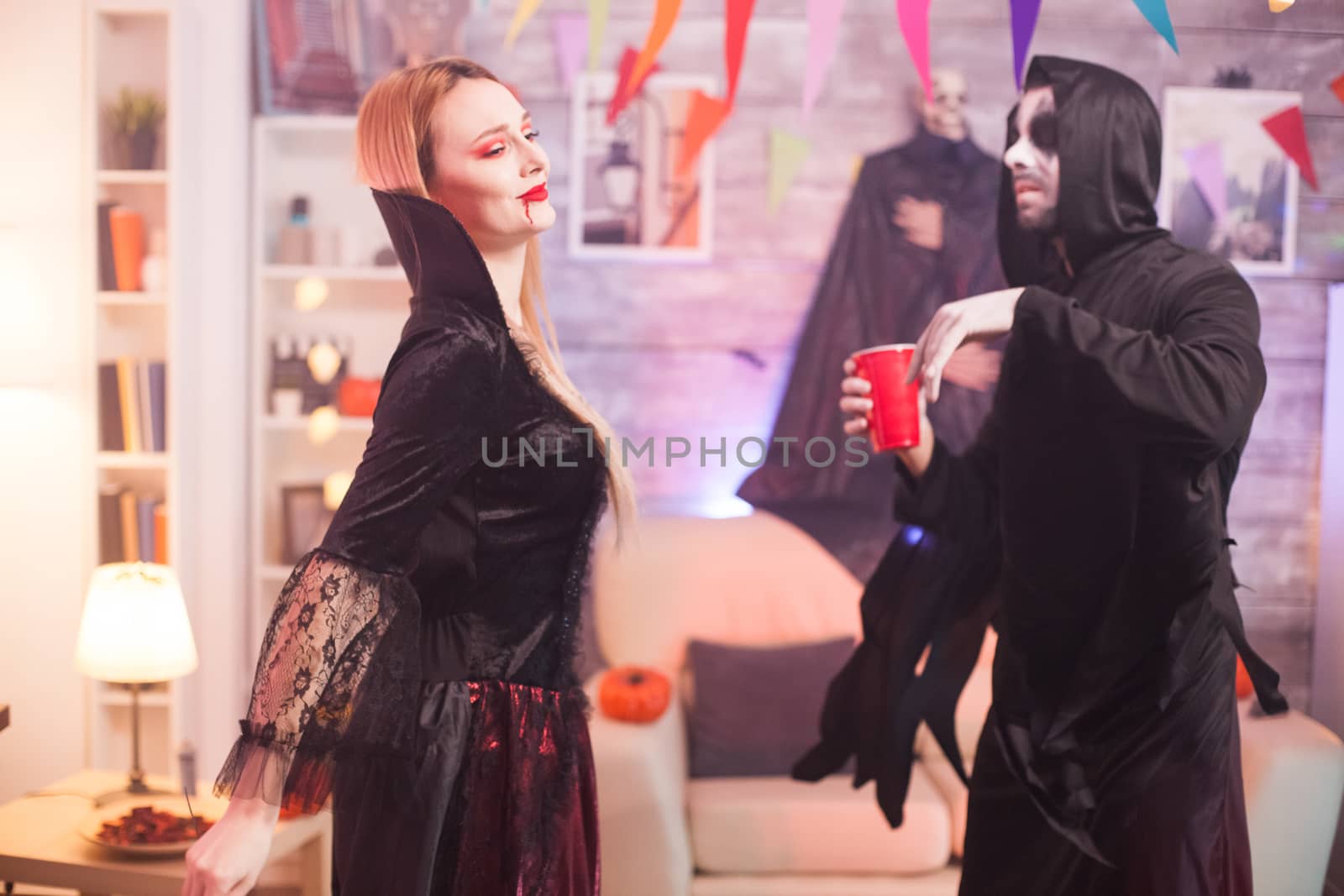 Man dressed up like a grim reaper dancing with beautiful vampire woman at halloween celebration.