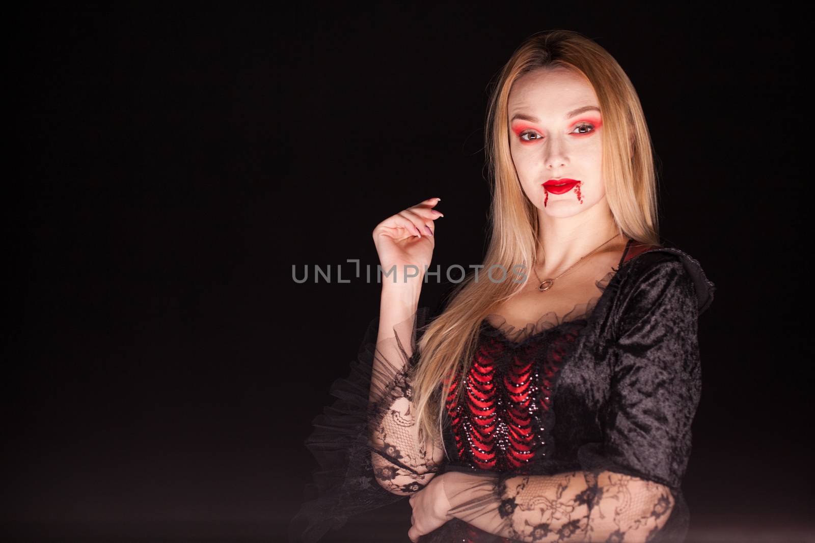 Lady of death with dripping blood from lips over black background. Halloween costume.