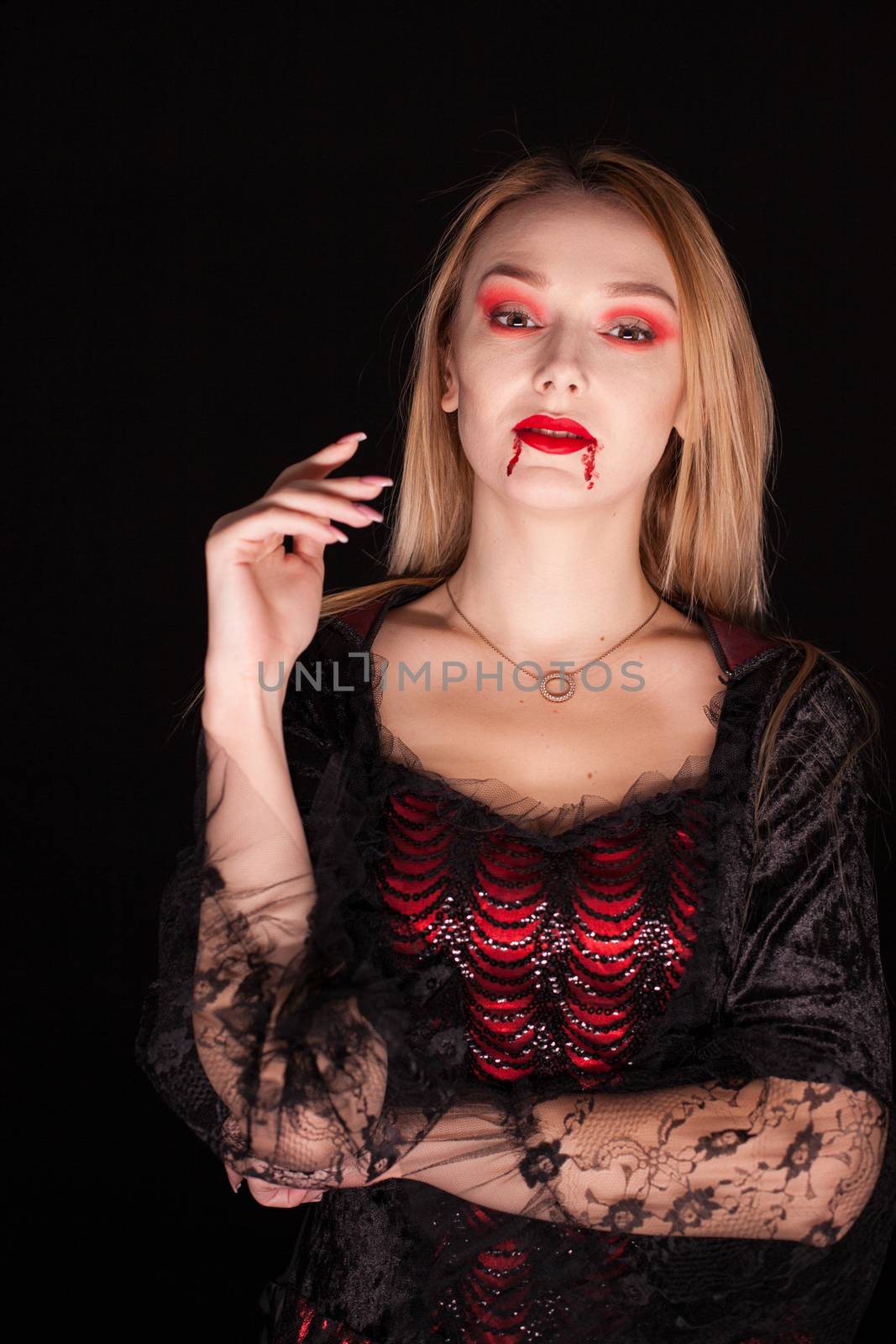 Young pretty woman with blood on his lips dressed up like a vampire for halloween over black background.