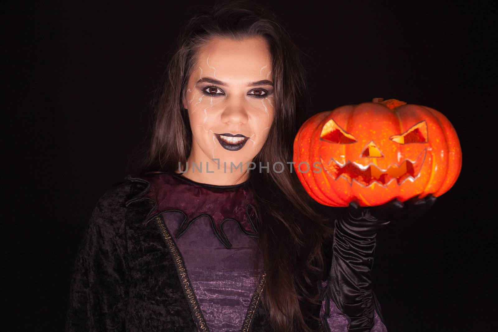 Lady in witch costume holding a pumpkin over black background for halloween.
