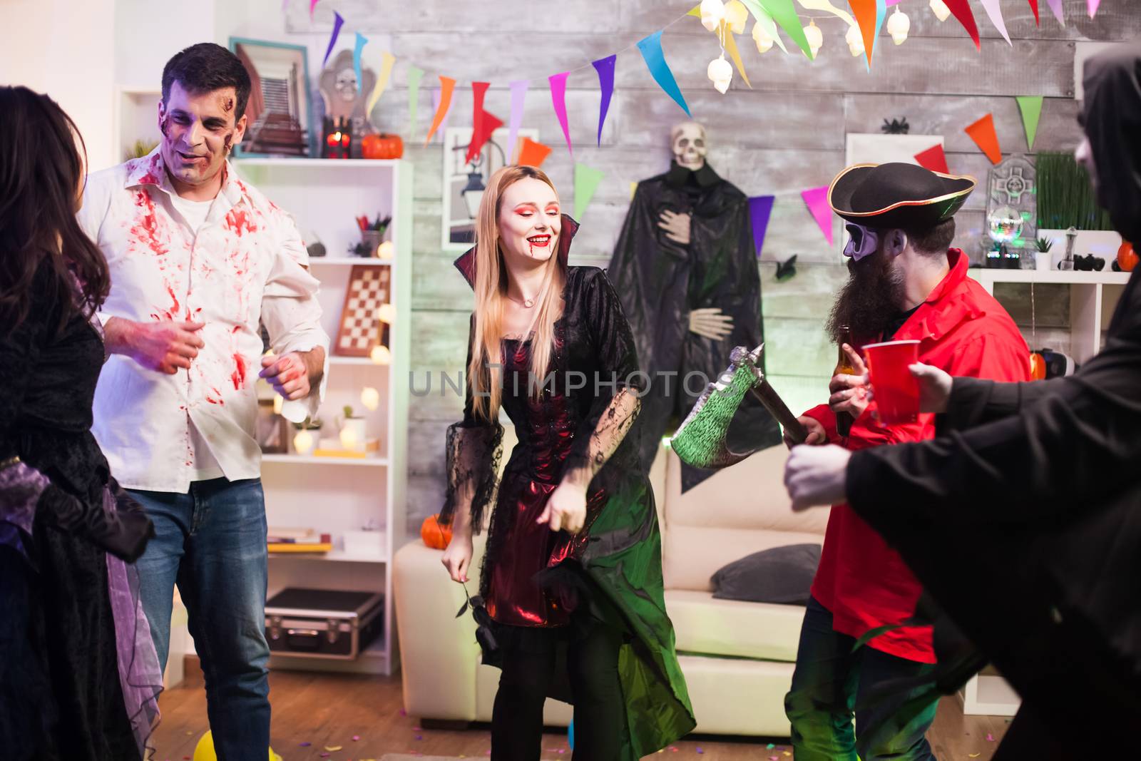 Beautiful woman dressed up like a vampire dancing with a pirate while holding his axe at halloween celebration.