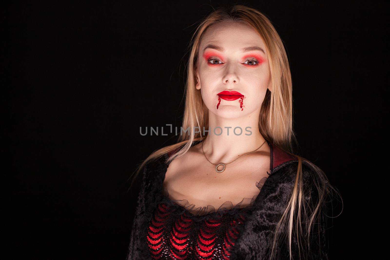 Beautiful vampire woman with dripping blood over black background.
