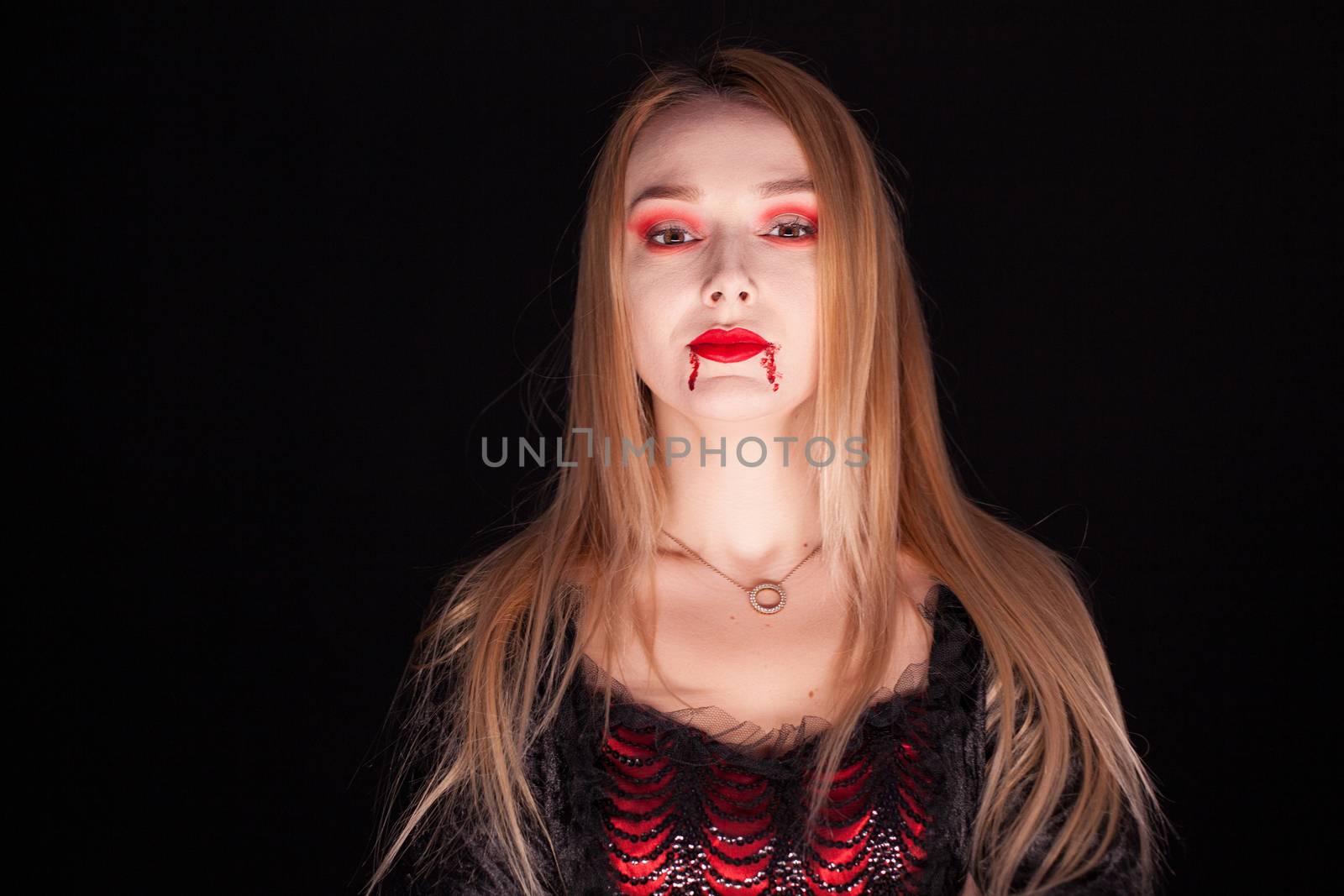 Beautiful blond woman dressed up like a vampire over black background.