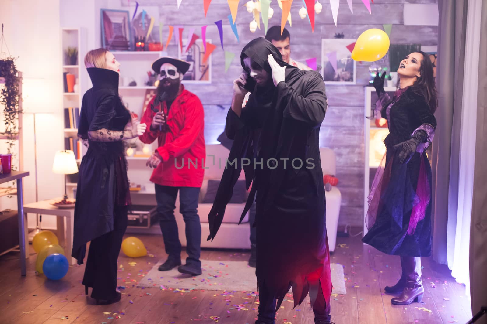 Man in grim reaper costume can't talking on the phone while celebrating halloween with his friends.
