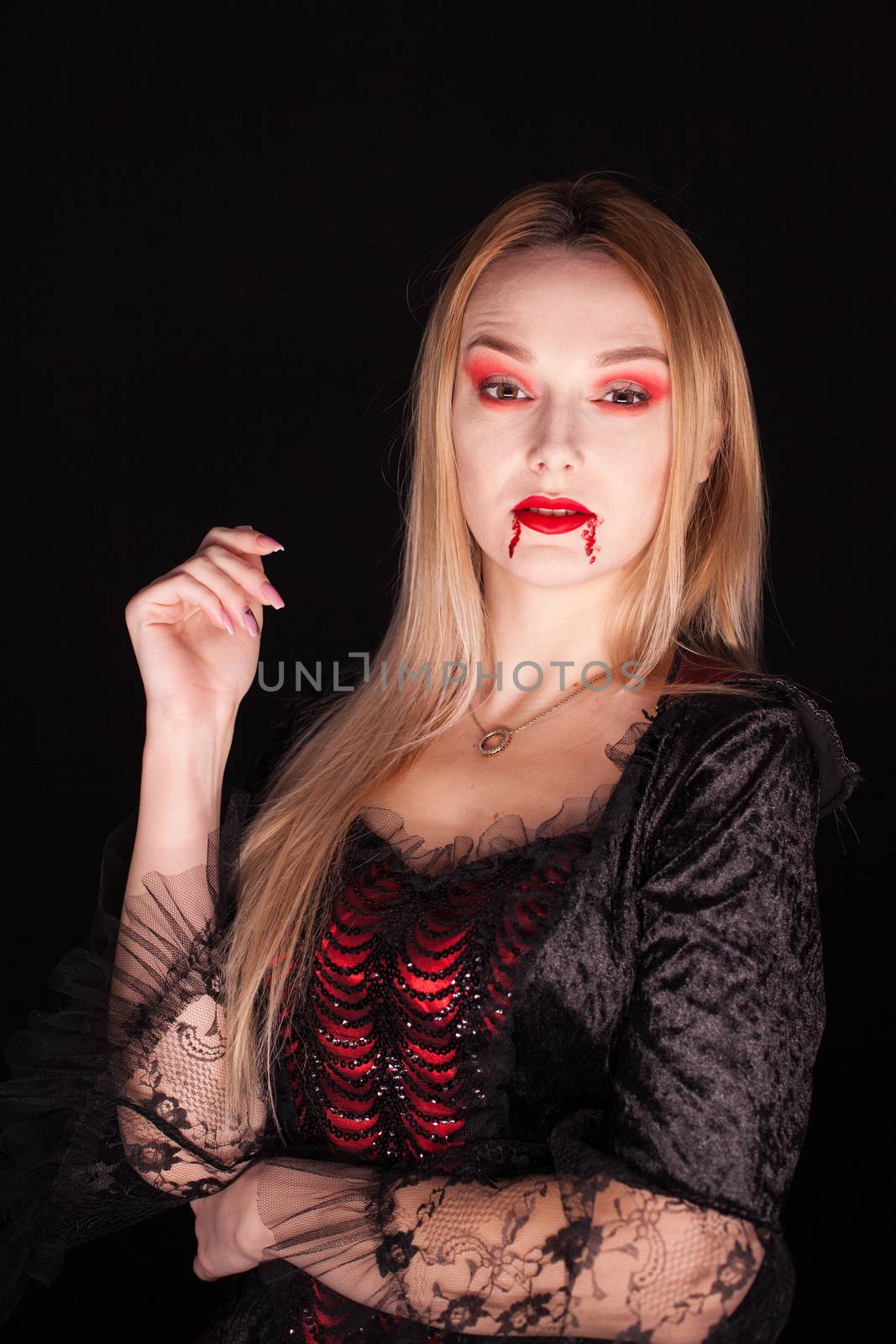 Caucasian girl dressed up like a vampire for halloween over black background.