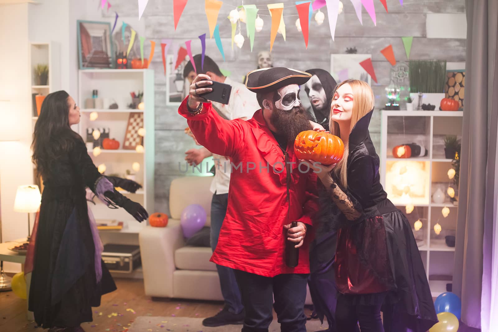 Bearded medieval pirate taking a selfie with beautiful vampire woman at halloween party. Spooky pumpkin.