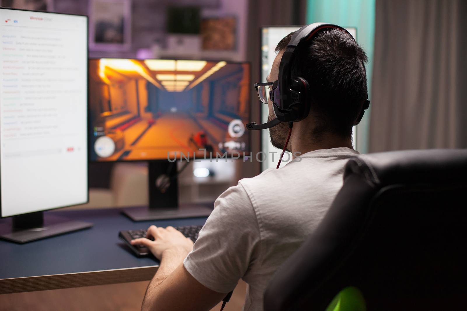 Man playing professional shooter game on his computer late at night in room with neon light.