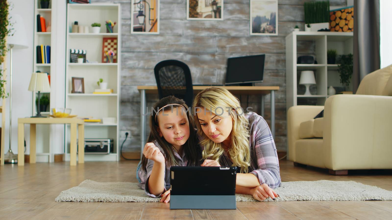 Cheerful little girl with her mother lying on the floor using tablet computer.
