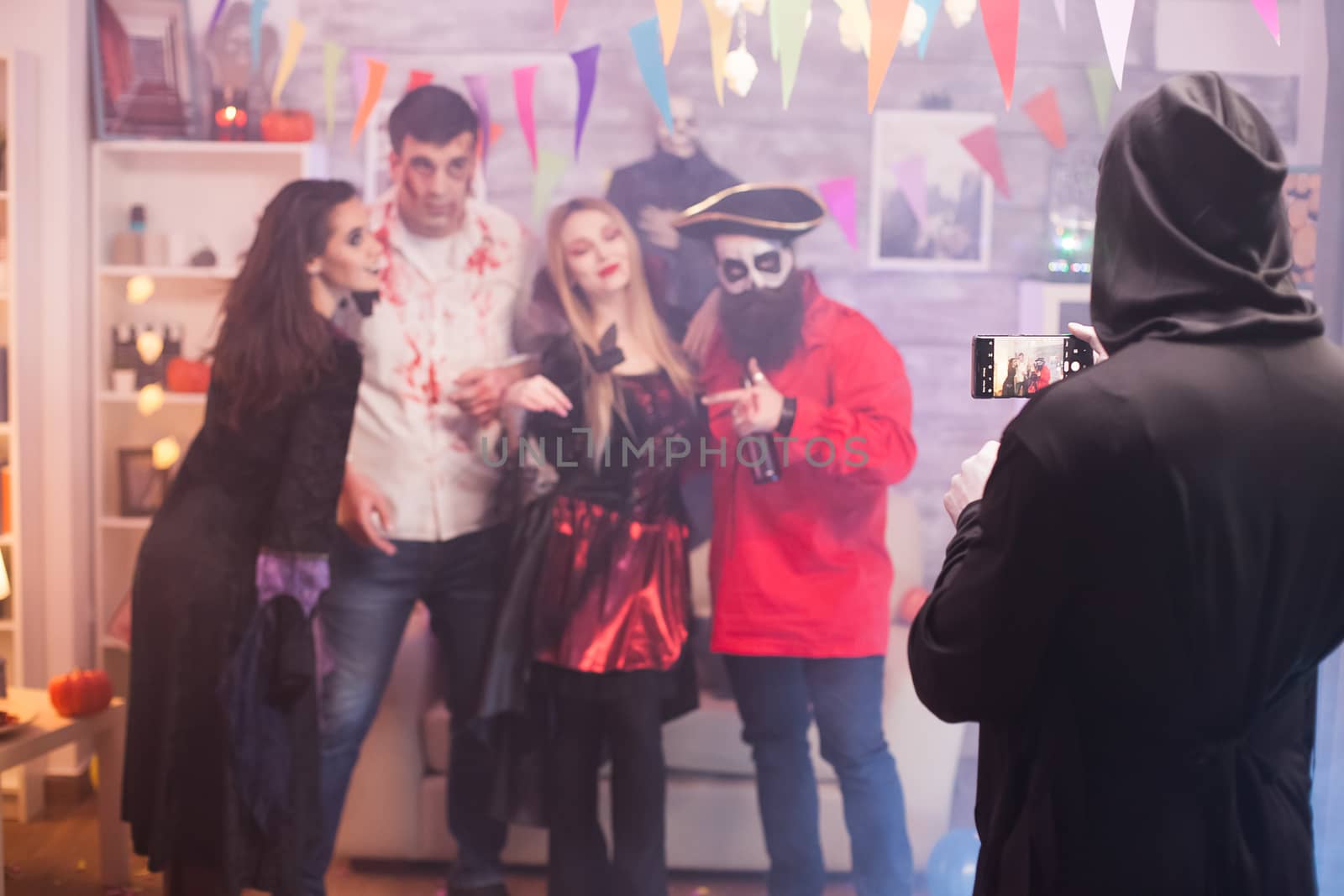 Back view of grim reaper taking a photo of friends at halloween party.