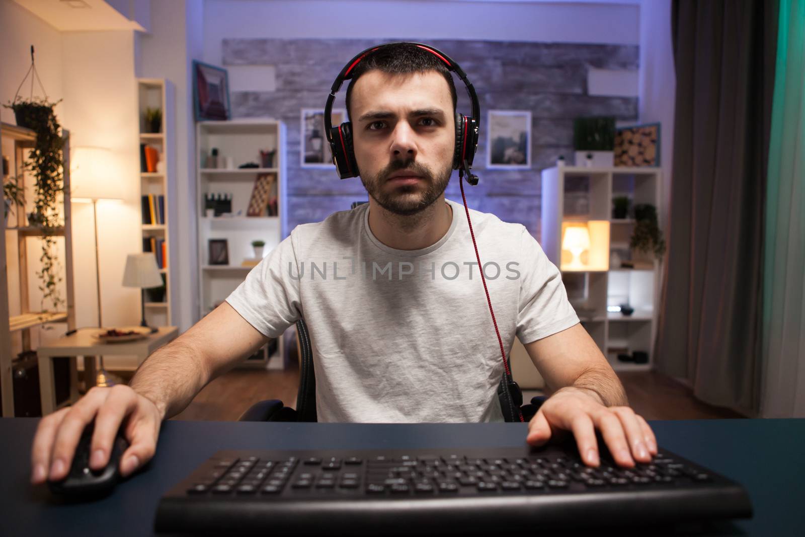 Pov of competitive young man playing online shooter games from his computer in a room with neon light. Man with headphones.