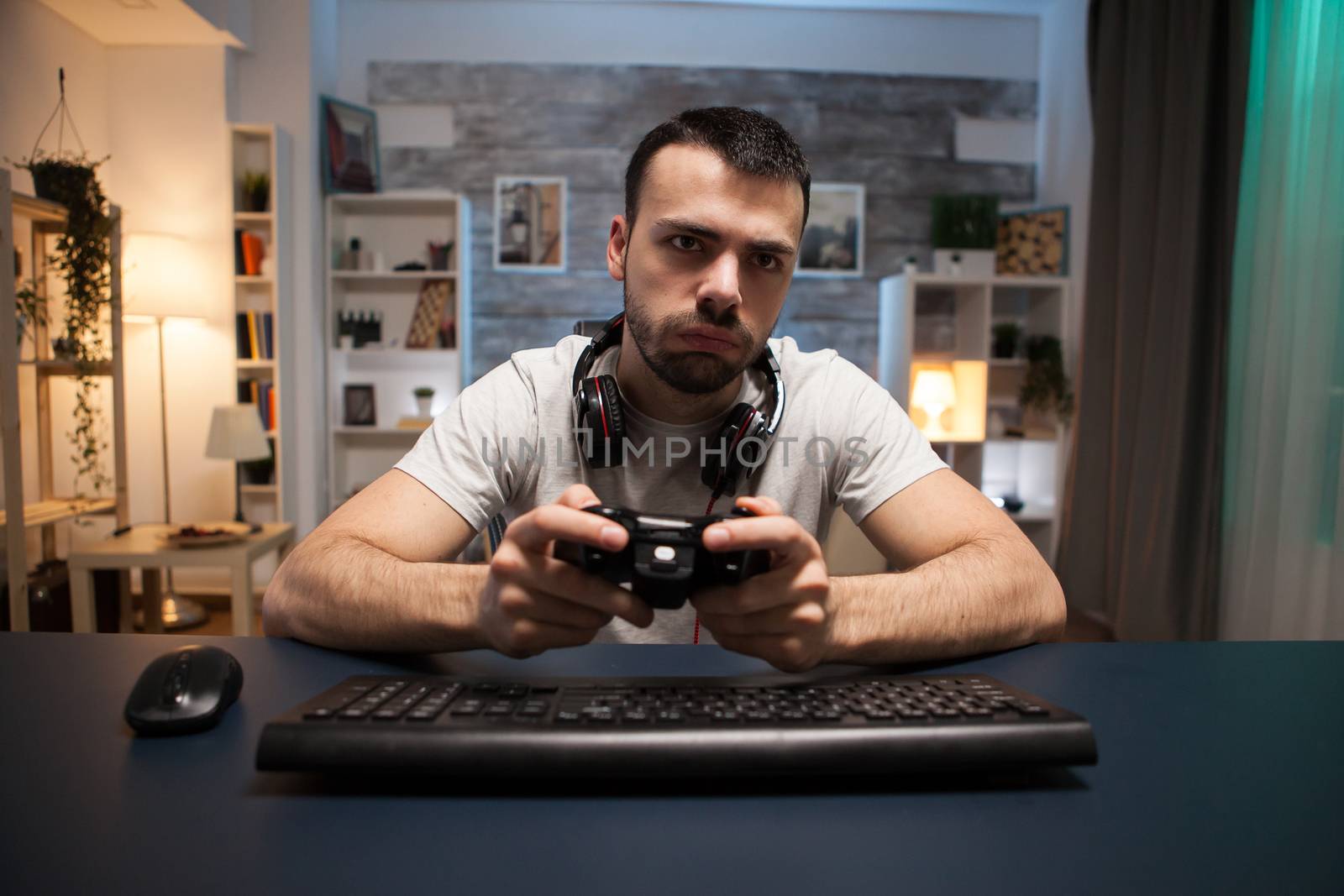 Pov of concentrated young man playing online shooter game on stream with wireless controller.