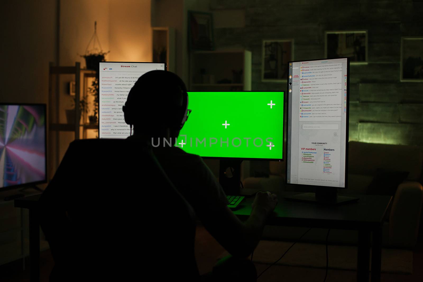 Back view of professional gamer playing on computer with green screen in a dark room.