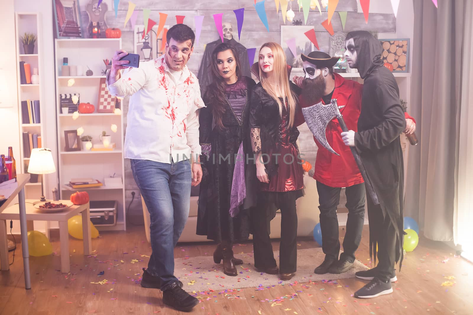 Group of friends looking into the camera and taking a selfie at halloween party in their costumes.