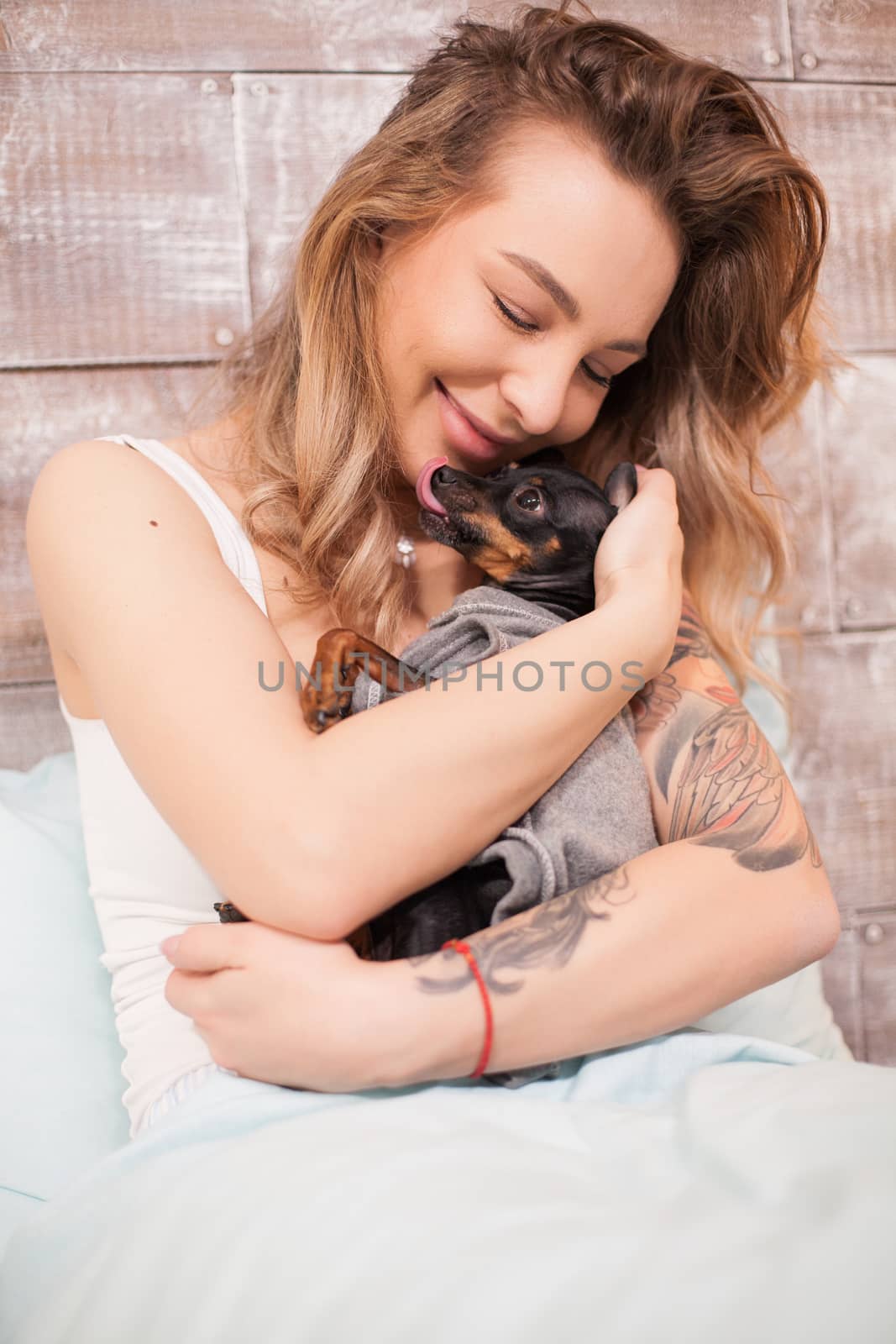 Pretty young woman in pajamas giving affection to her little dog. Happy adult.