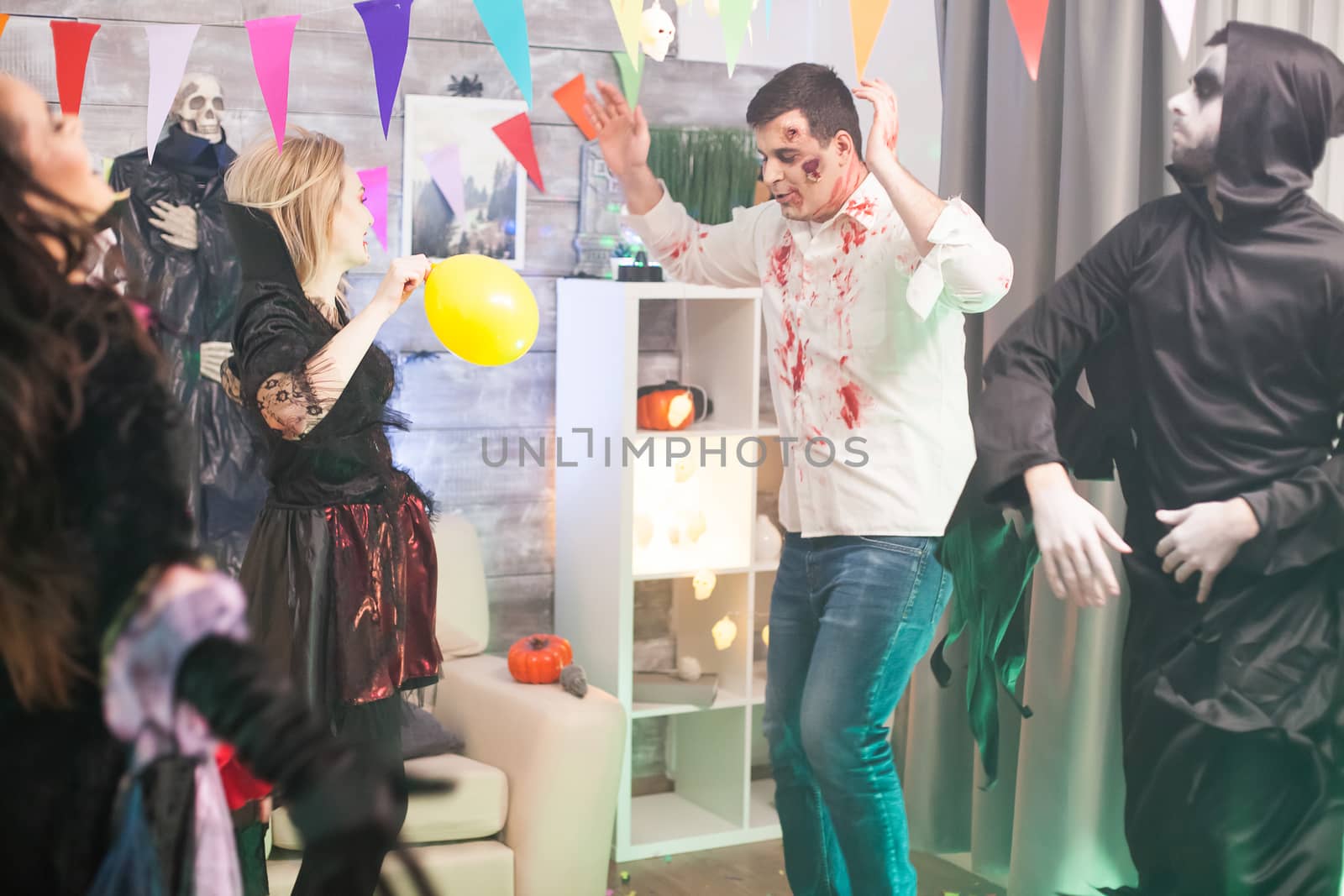 Bloody zombie and grim reaper dancing with hands up at halloween celebration.