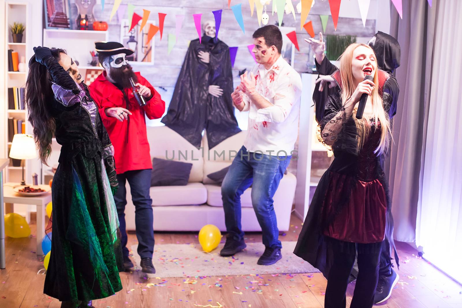 Beautiful woman dressed up like a vampire doing karaoke at halloween party with her friends.