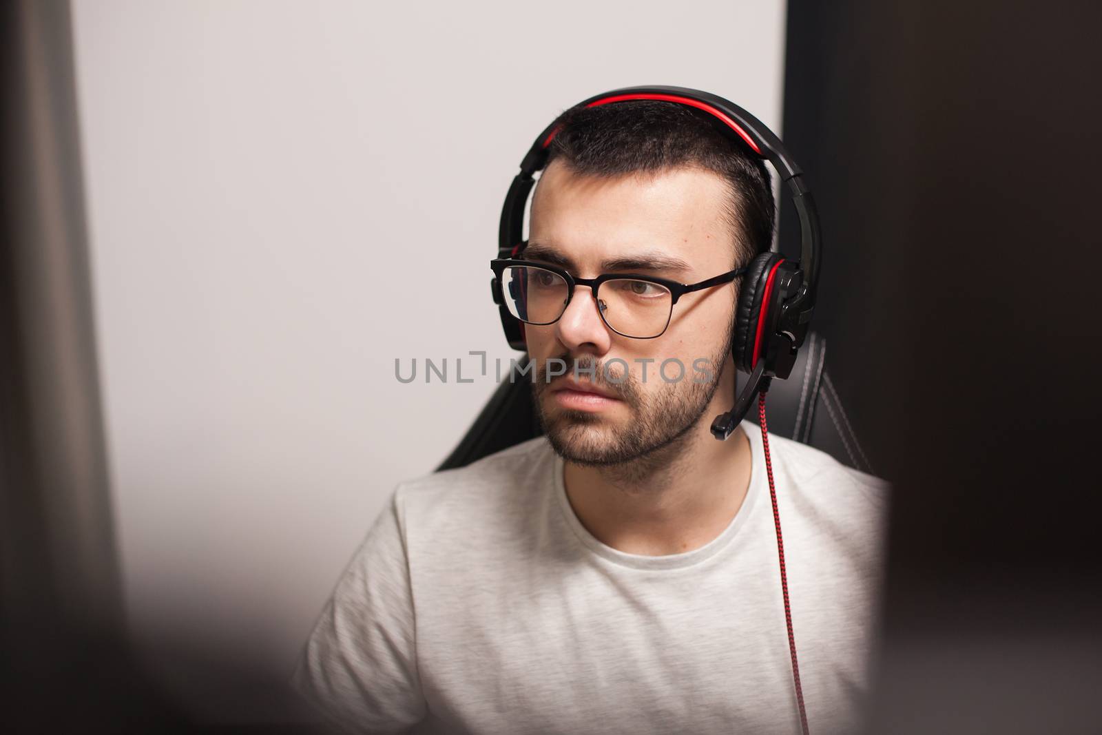 Portrait of young man with eyeglasses wearing headset while playing games on computer.