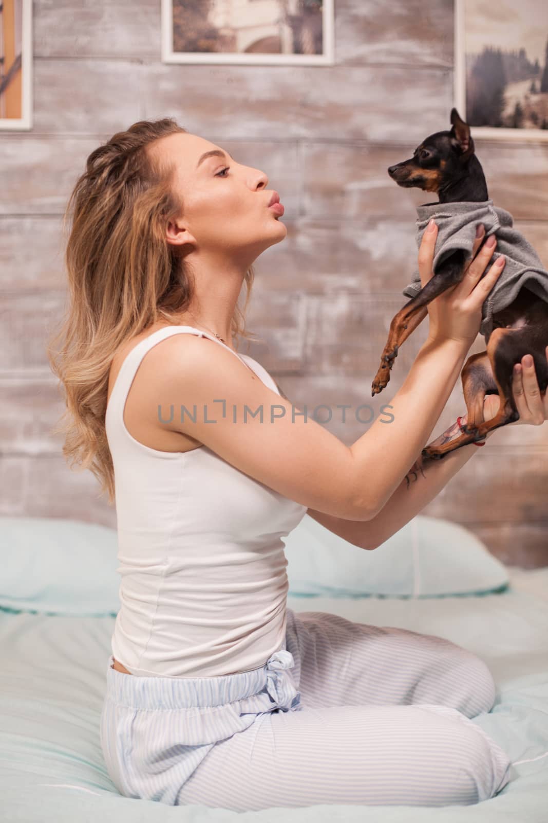 Blonde beautiful woman in her pajamas at night having fun with her dog on bed.