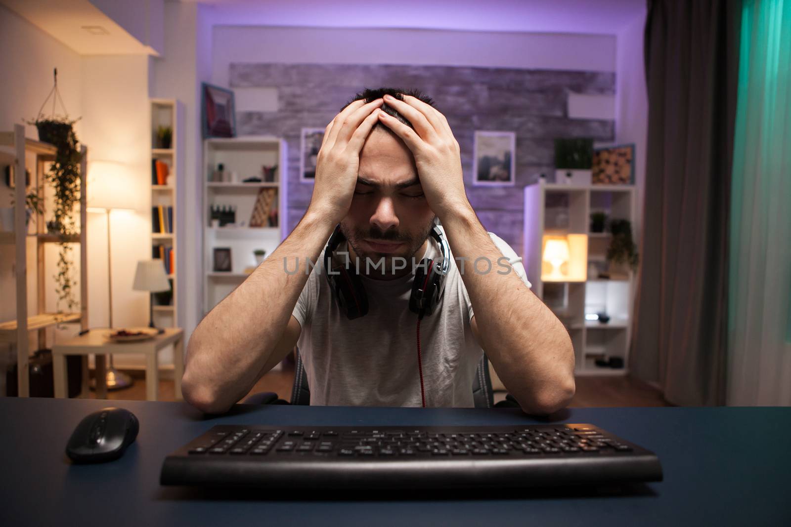 Pov of young man covering his face with his hands after losing at online shooter game.