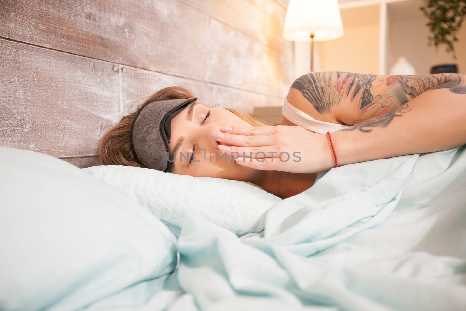 Beautiful young woman yawning while falling asleep in bedroom.