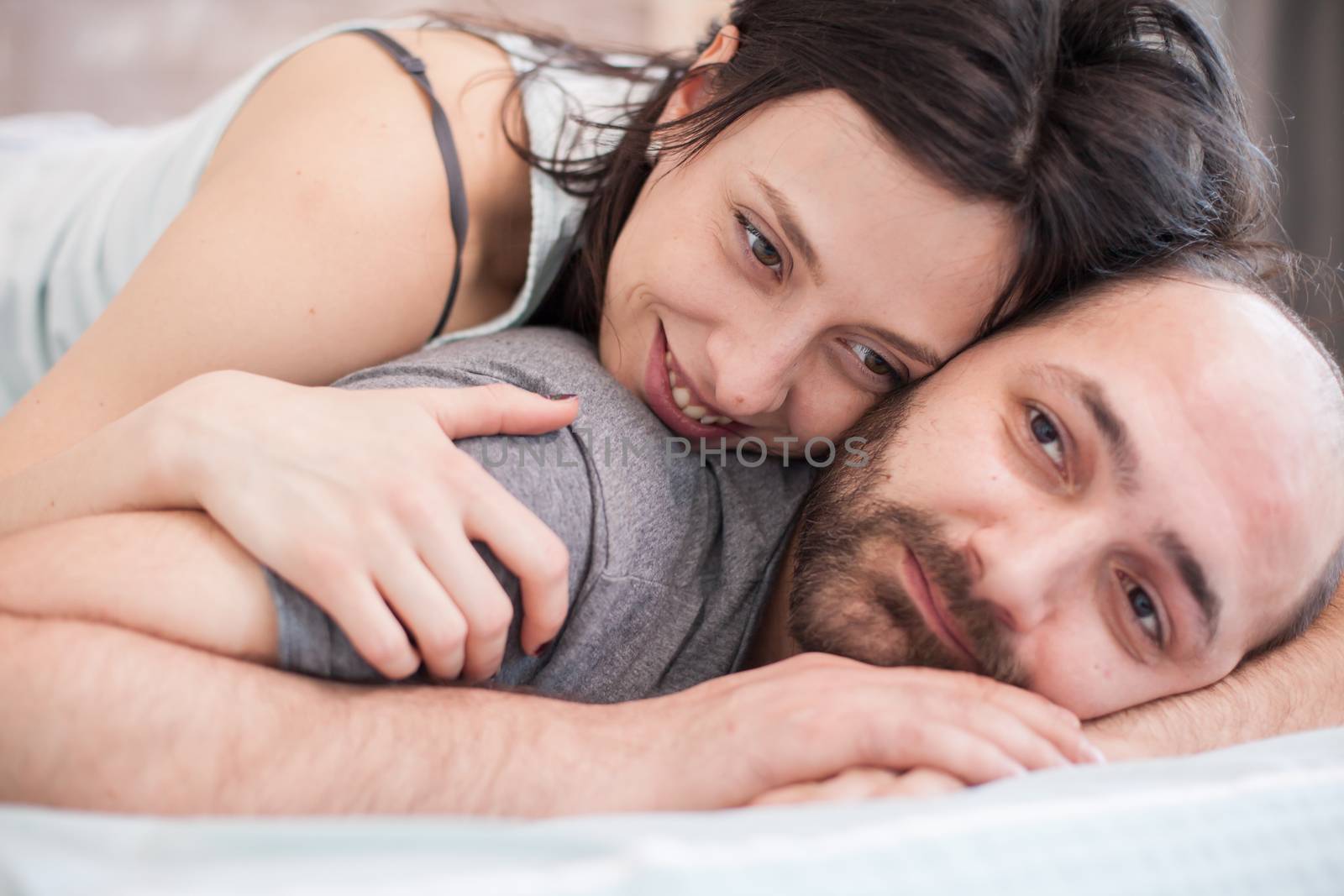 Close up of beautiful woman smiling after waking up in the morning and laying on her boyfriend back.