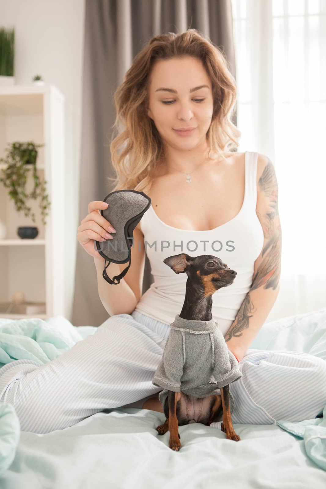 Lovely young woman in the morning playing with her dog in bed.