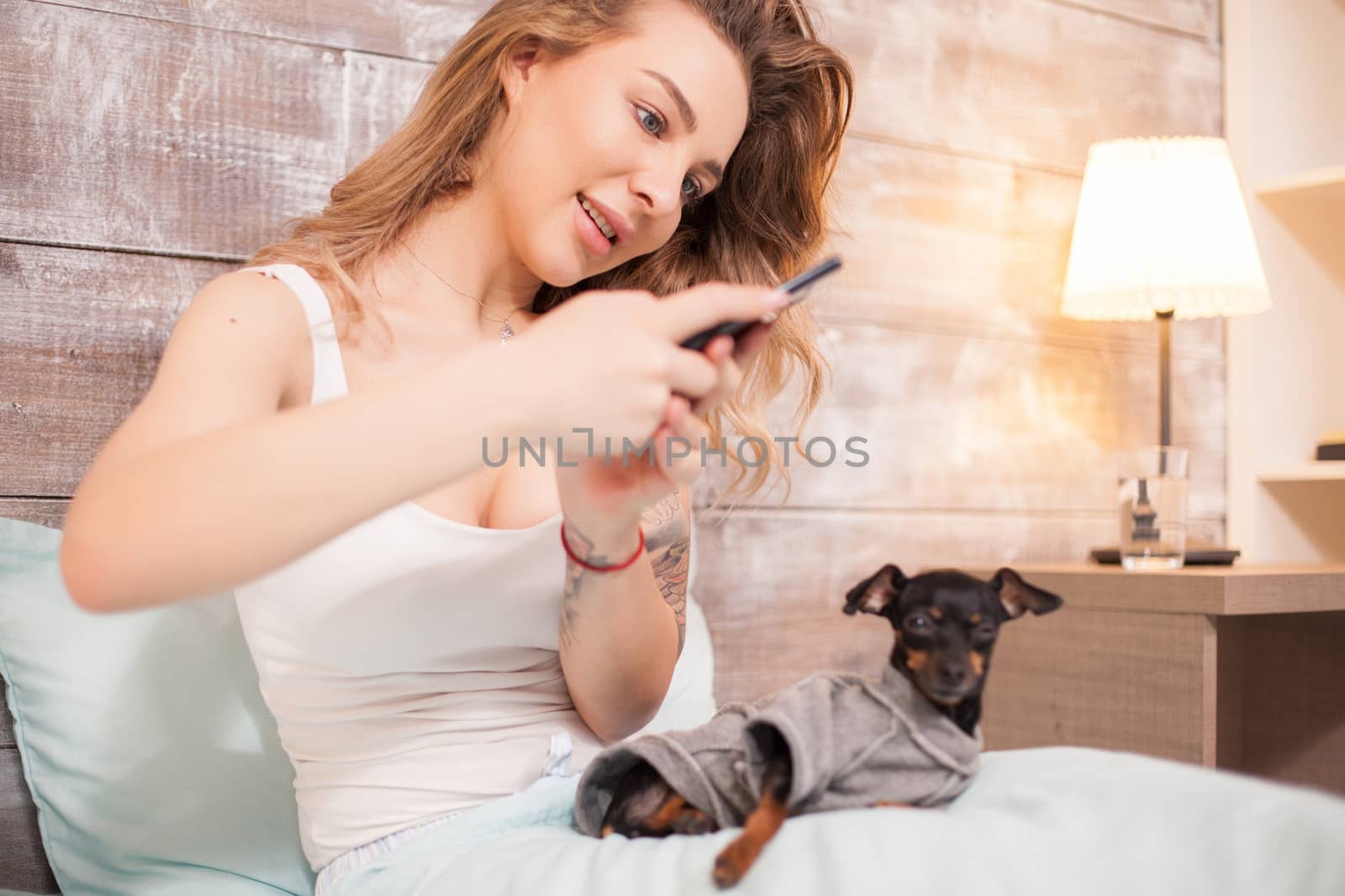 Young woman in pajamas taking a photo of her little dog by DCStudio