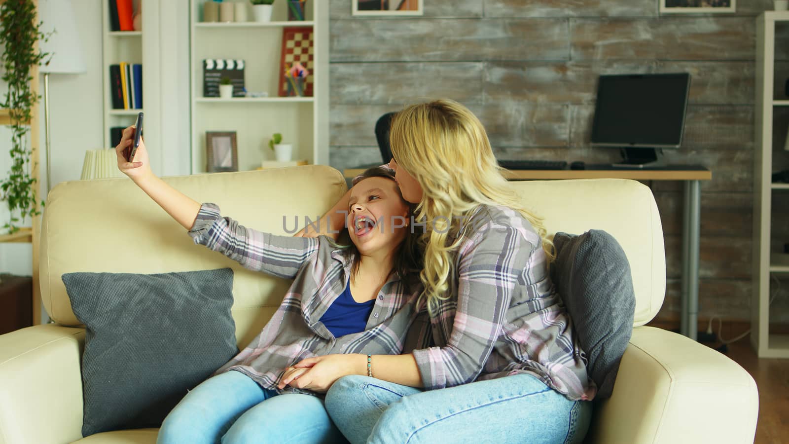 Cheerful mother and daughter taking a selfie with smartphone in living room.