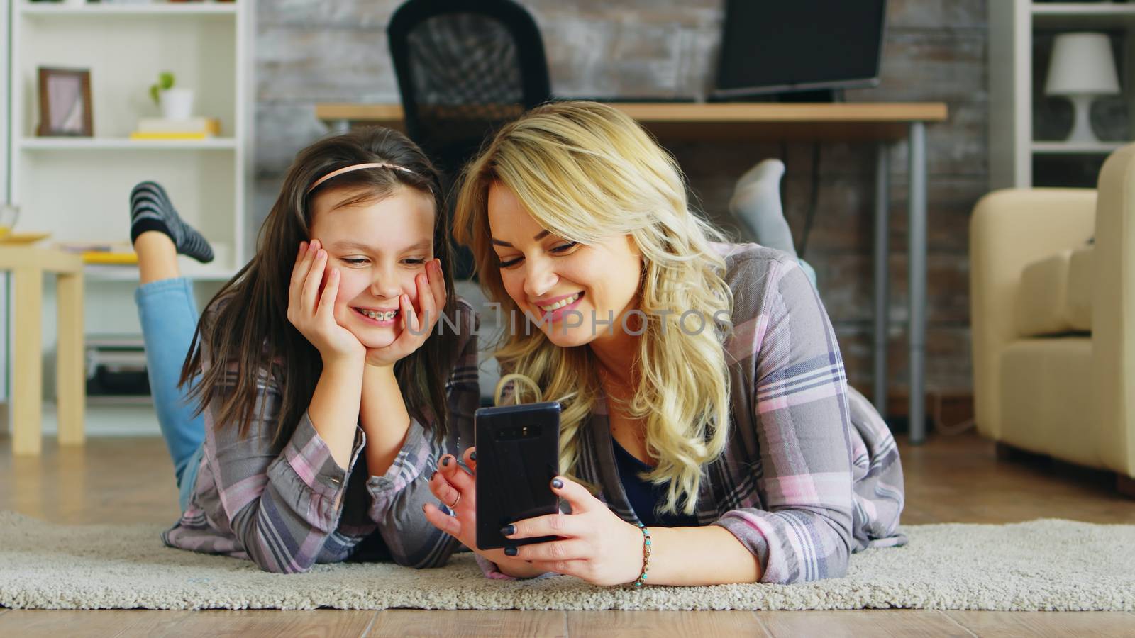 Little girl and her mother lying on the floor using smartphone for shopping.