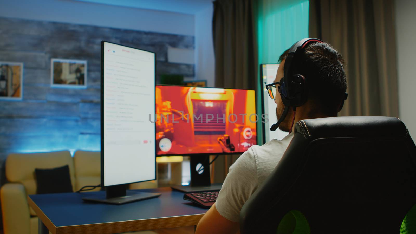 Young man with headphones talking on chat while playing shooter games on powerful PC