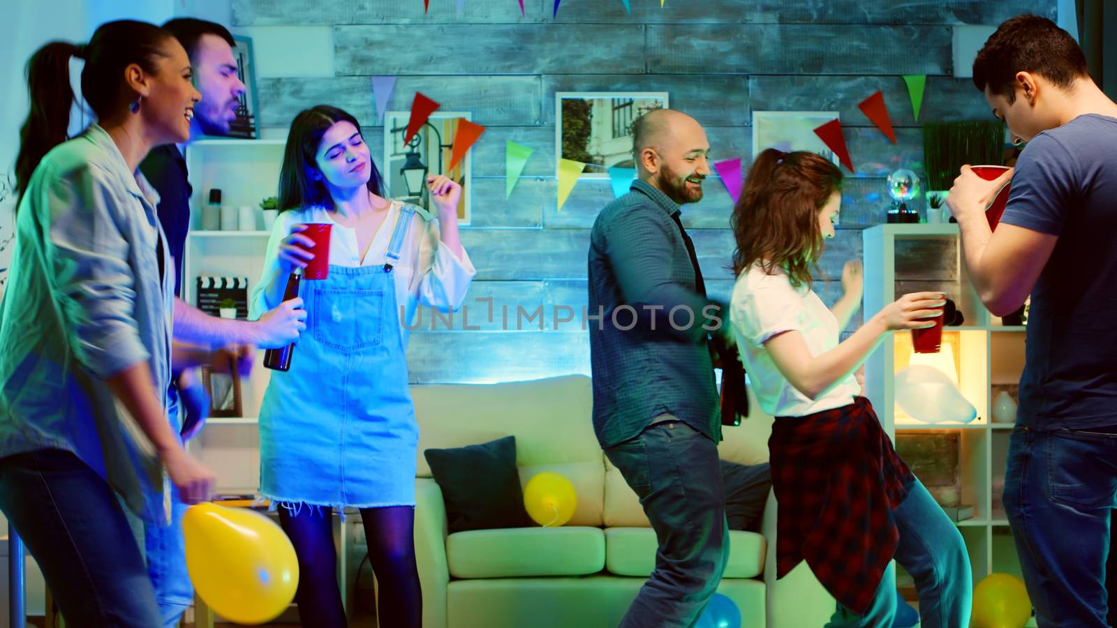 Bald attractive young man smiling while dancing at the party with his friends. Wild college party with neon lights and disco ball