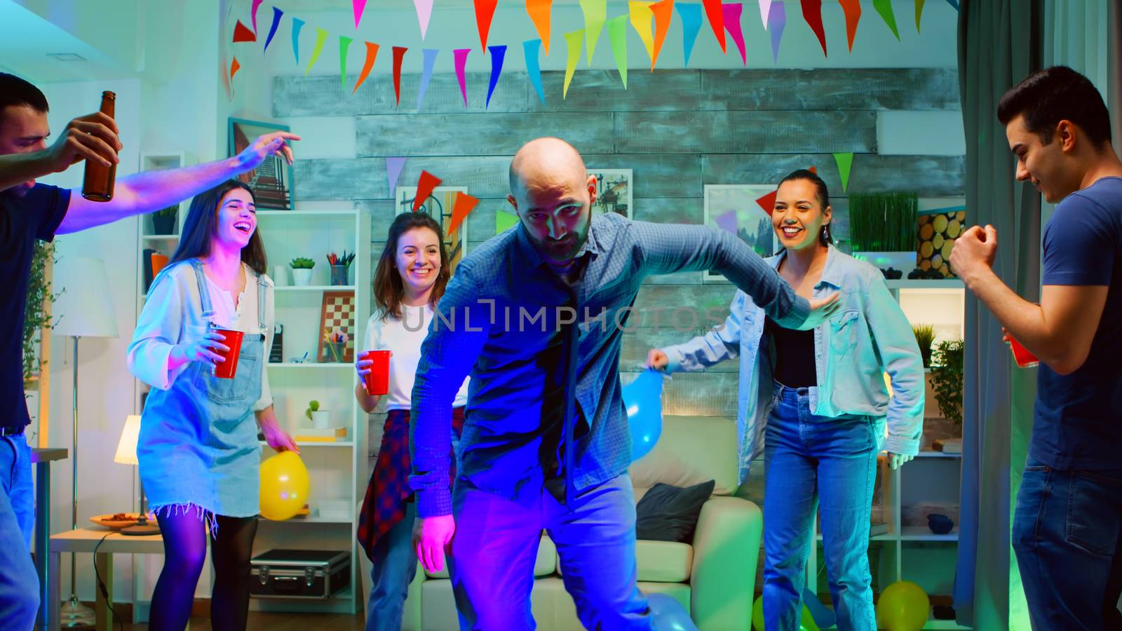 Handsome young man showing his dancing moves to her friends at the party in an apartment with neon lights. Robot dance at a wild disco party