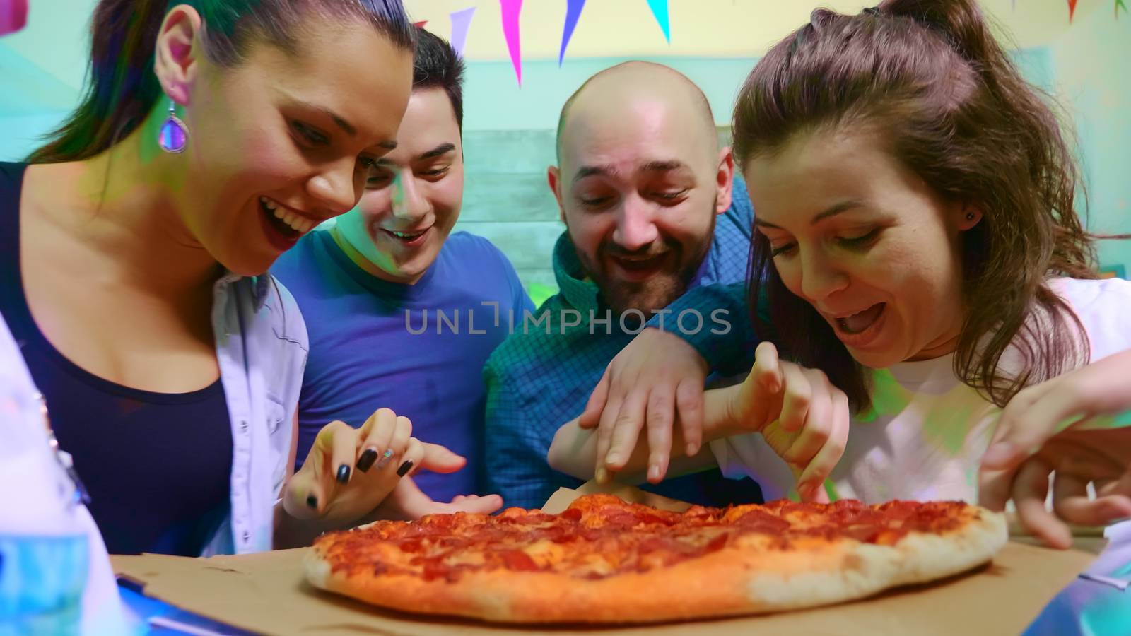 Group of young people full of excitement at arriving of pizza. Friends hangout at wild college party with neon lights