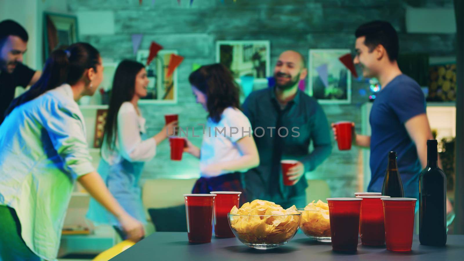 Chips and cups with beer on the table with people dancing in the background at the party.