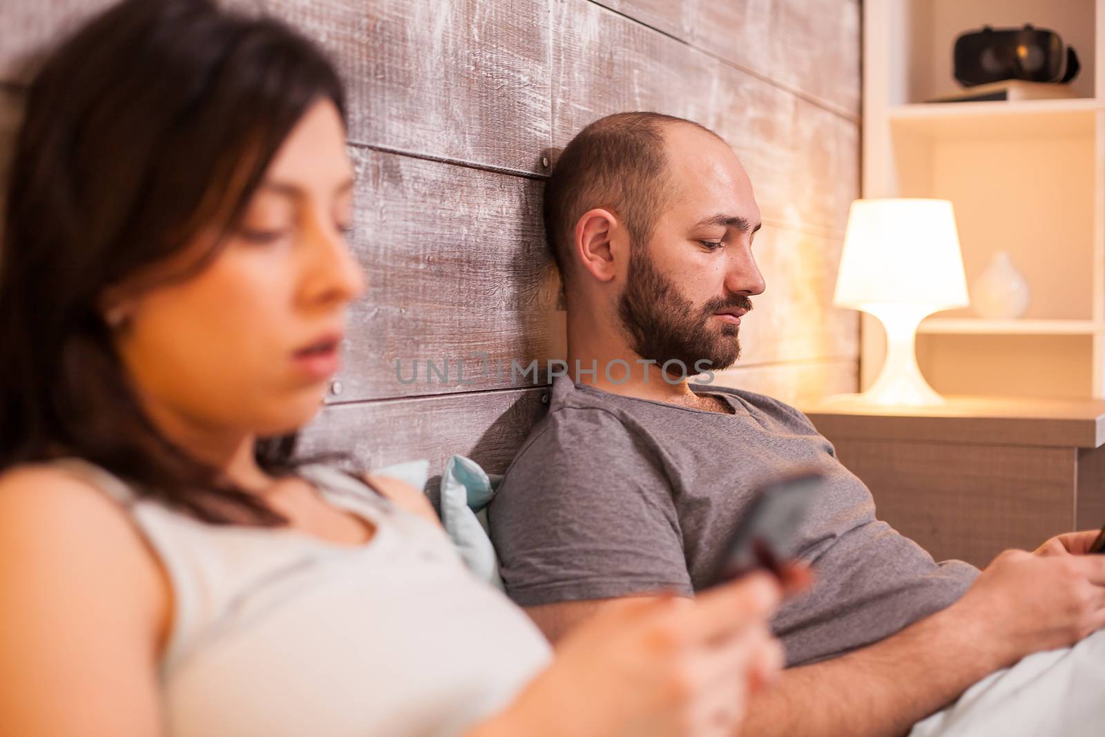 Distant couple in bed before bedtime using smartphone.