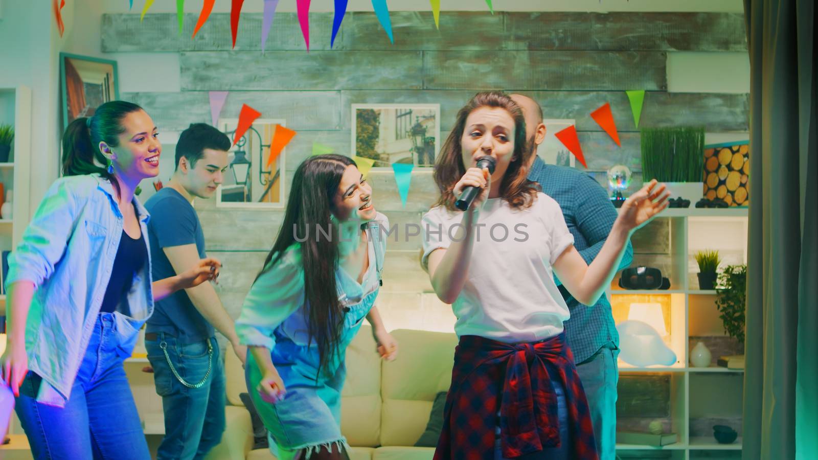 Attractive young woman doing karaoke at the party while her friends are cheering for her.