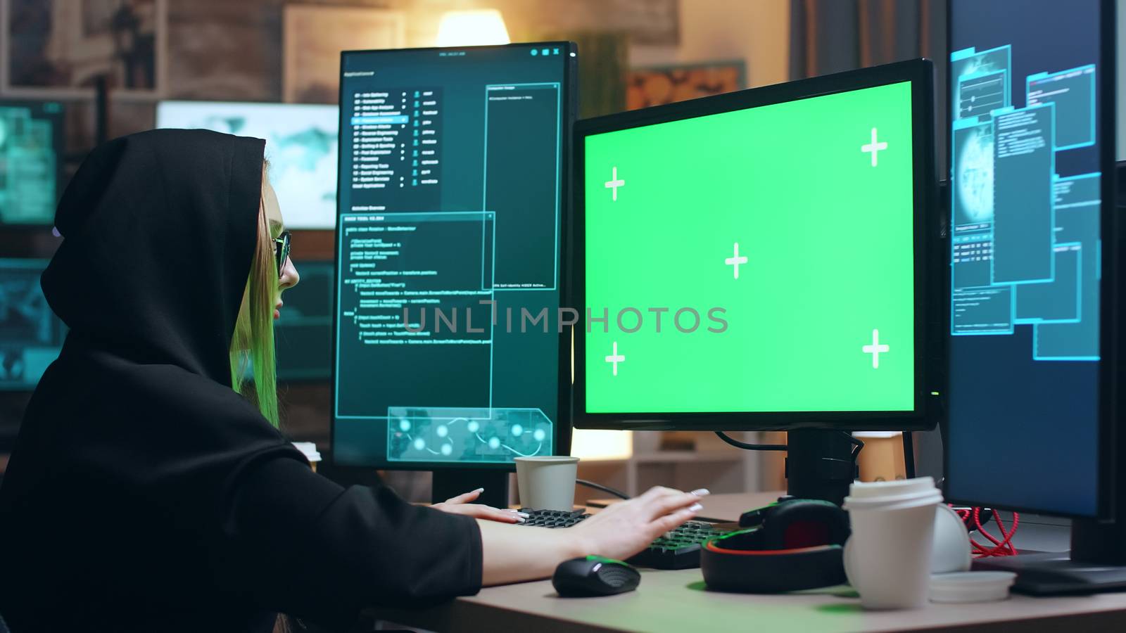 Female cyber terrorist wearing a hoodie working on computer with green screen.