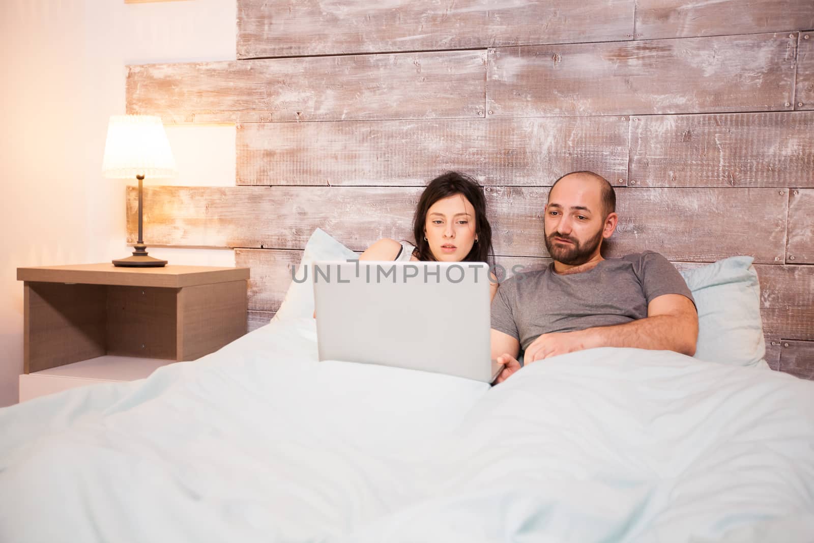 Young married couple in pajamas spending time at home using laptop.