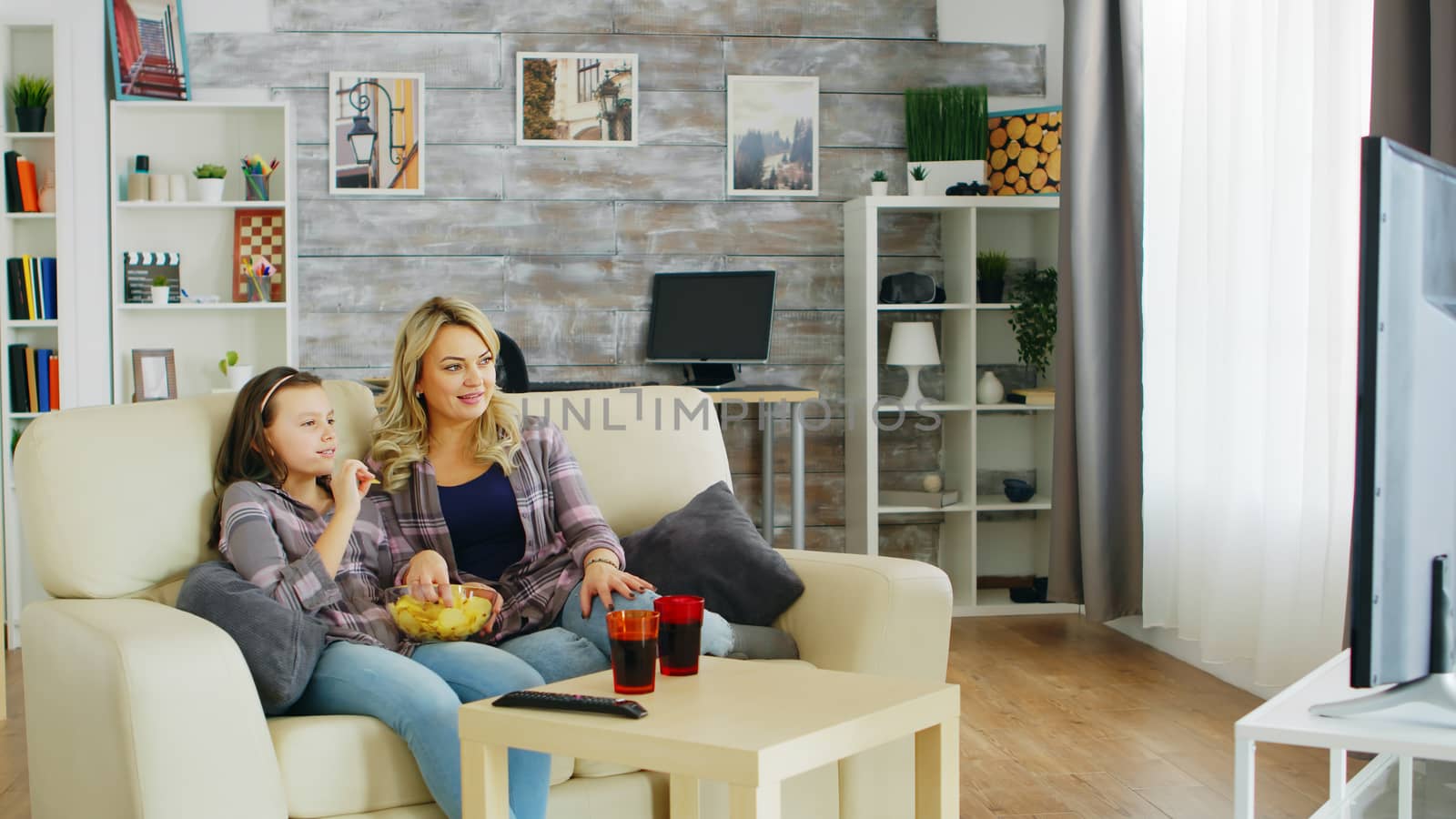 Beautiful young mother and her daughter watching tv by DCStudio