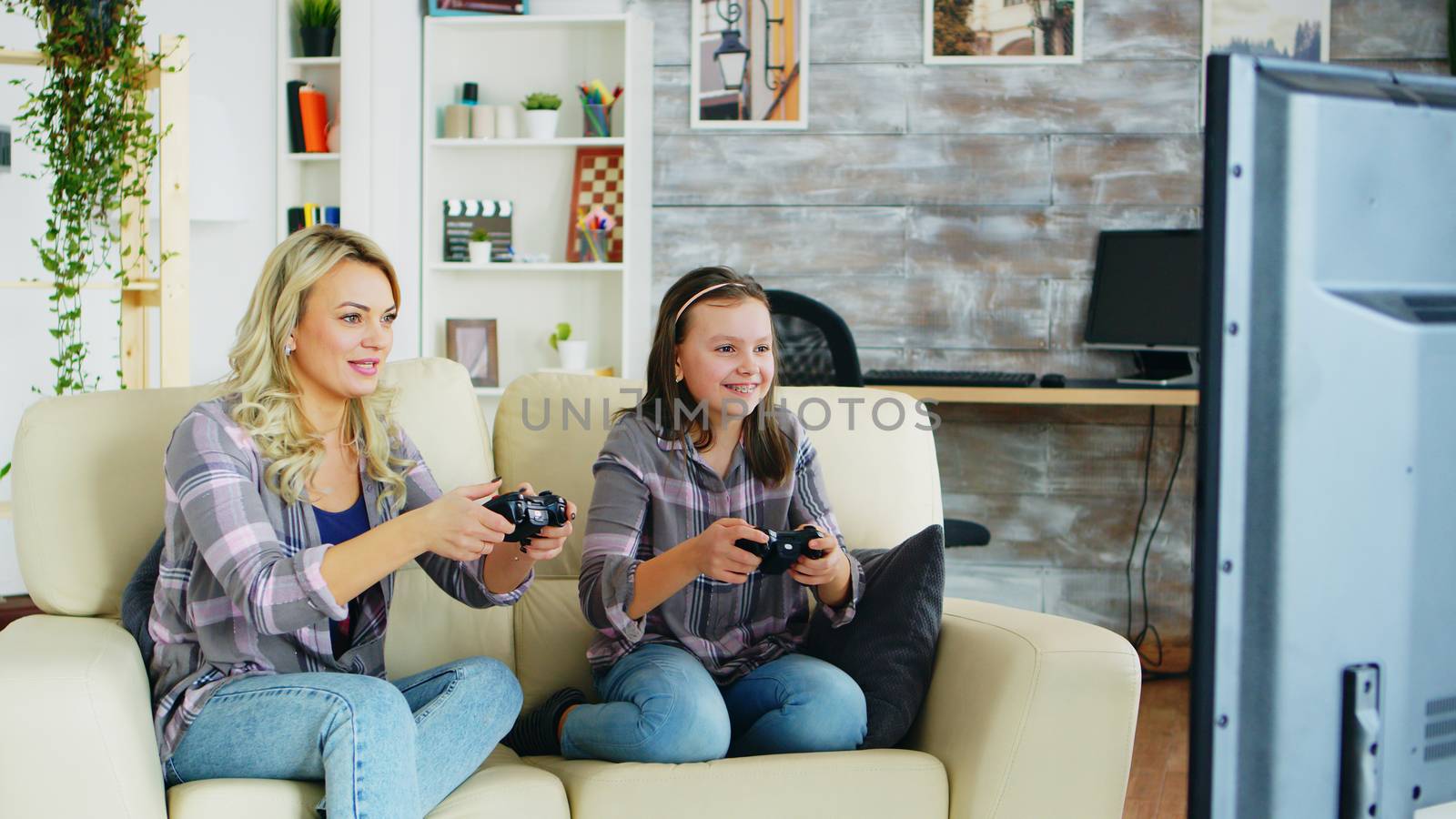 Beautiful young mother playing video games with her daughter by DCStudio