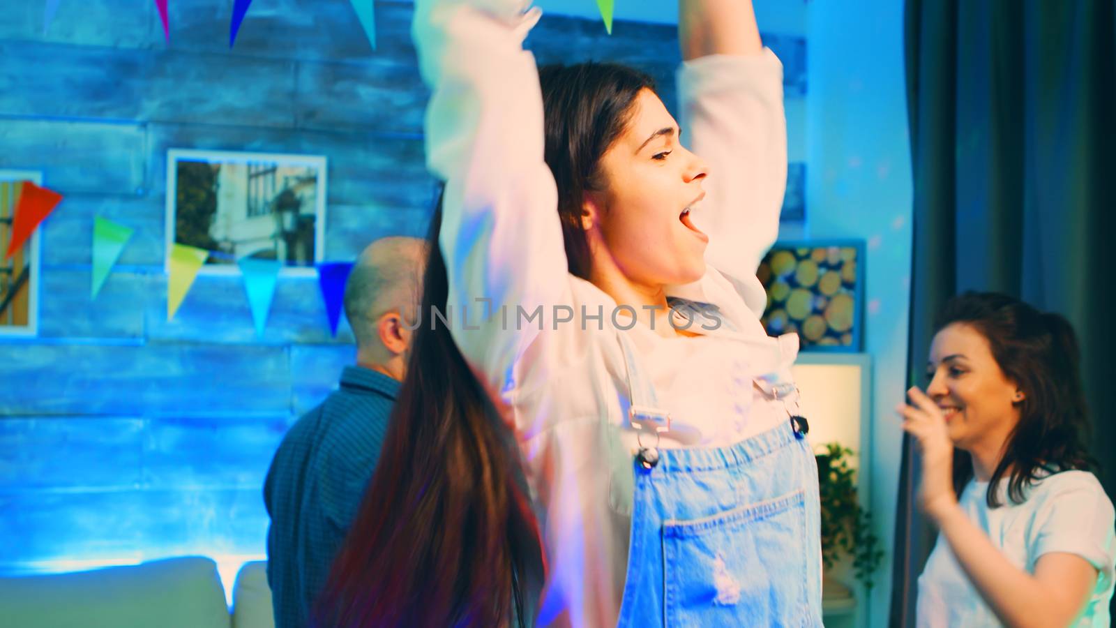 Attractive young woman dancing at the party with her friends. Group of people partying. Handheld slow motion shot