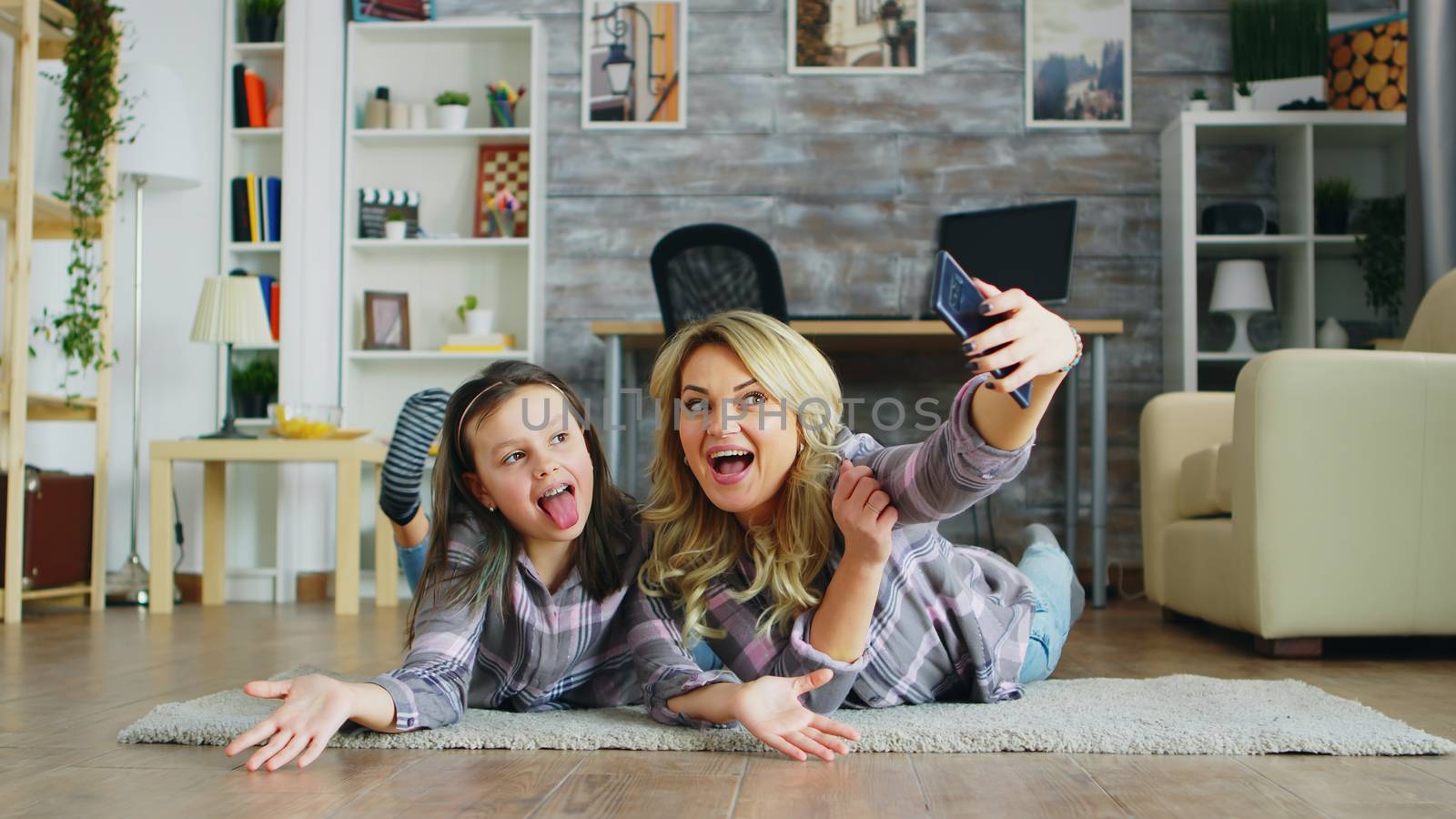 Mother and daughter lying on the floor taking a selfie with smartphone.